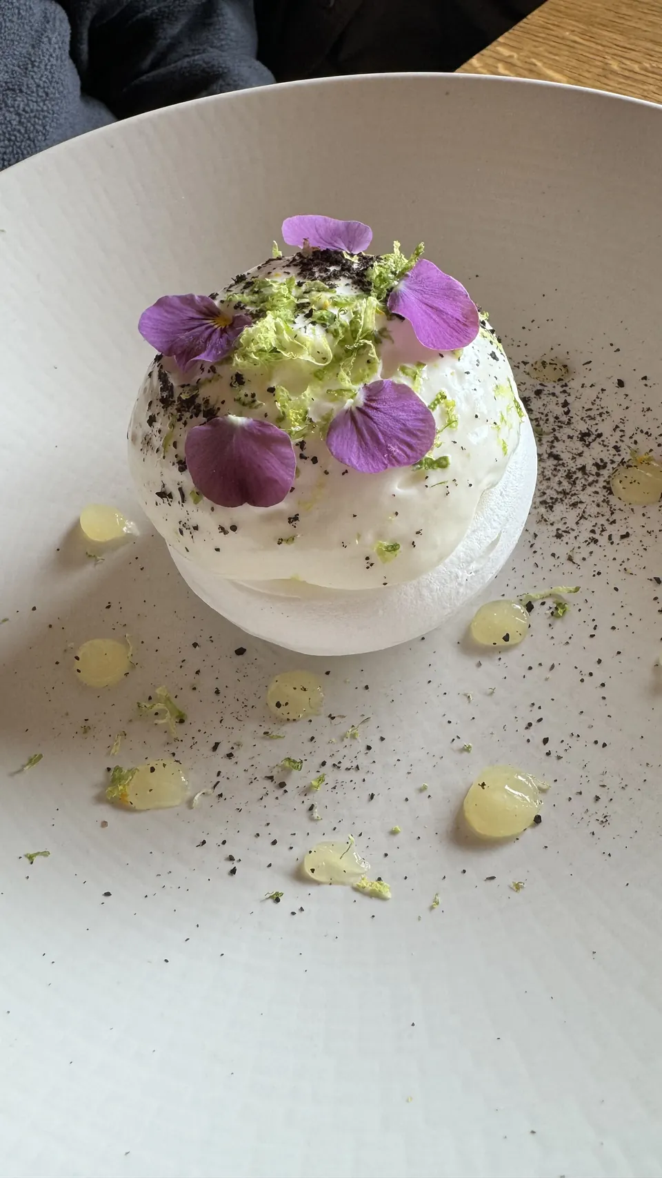 Dessert blanc décoré de fleurs violettes et de zestes, dressé dans une assiette
